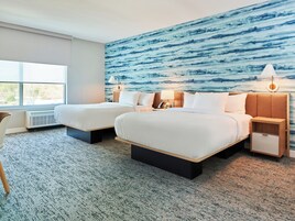 Habitación de hotel con dos camas, un ventanal grande, un mural en la pared y un escritorio con una silla.