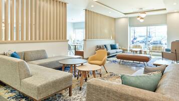 Een moderne hotellobby met banken, fauteuils en ronde tafels.