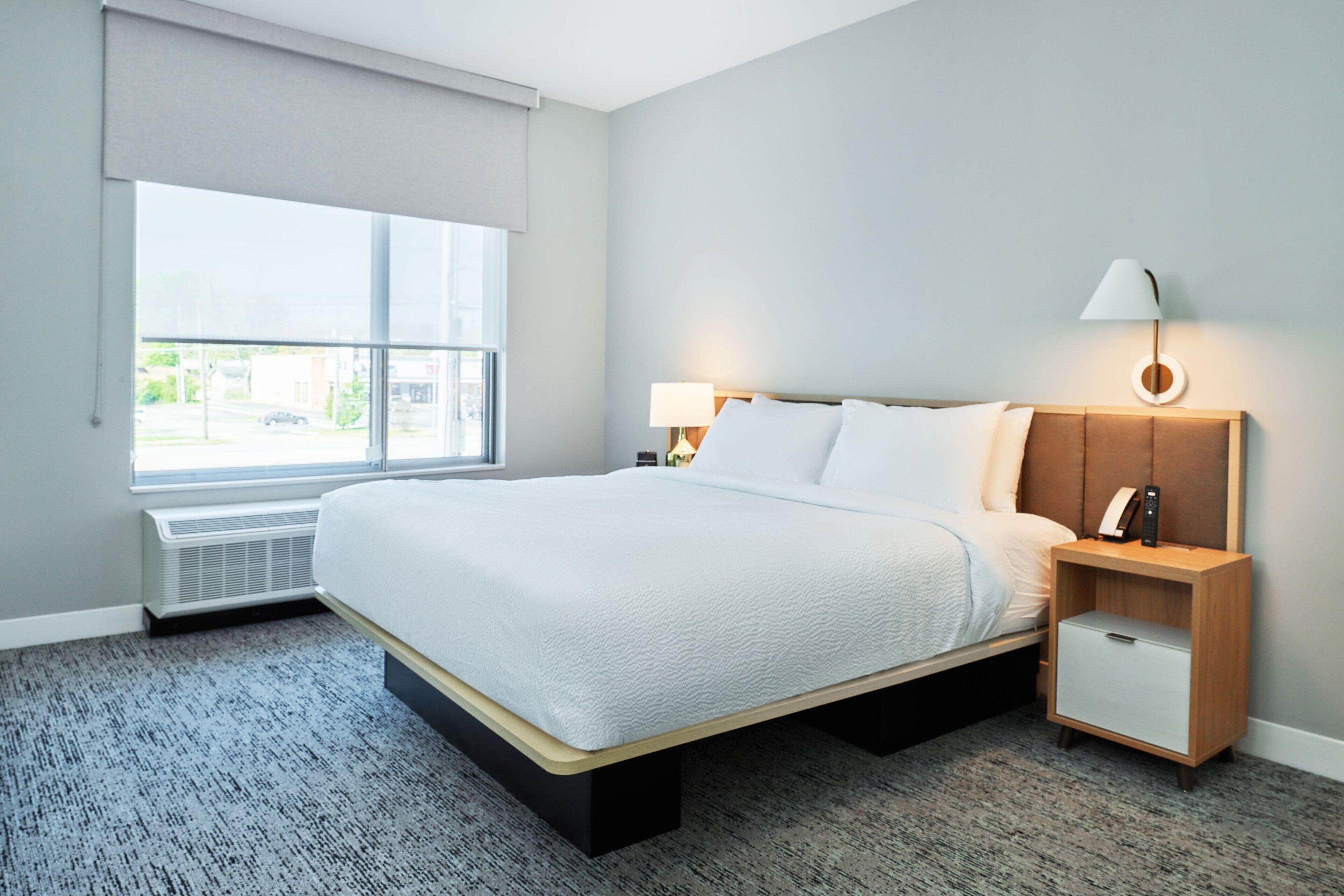 A hotel room with a large bed, bedside tables, a lamp, and a view of the outside.