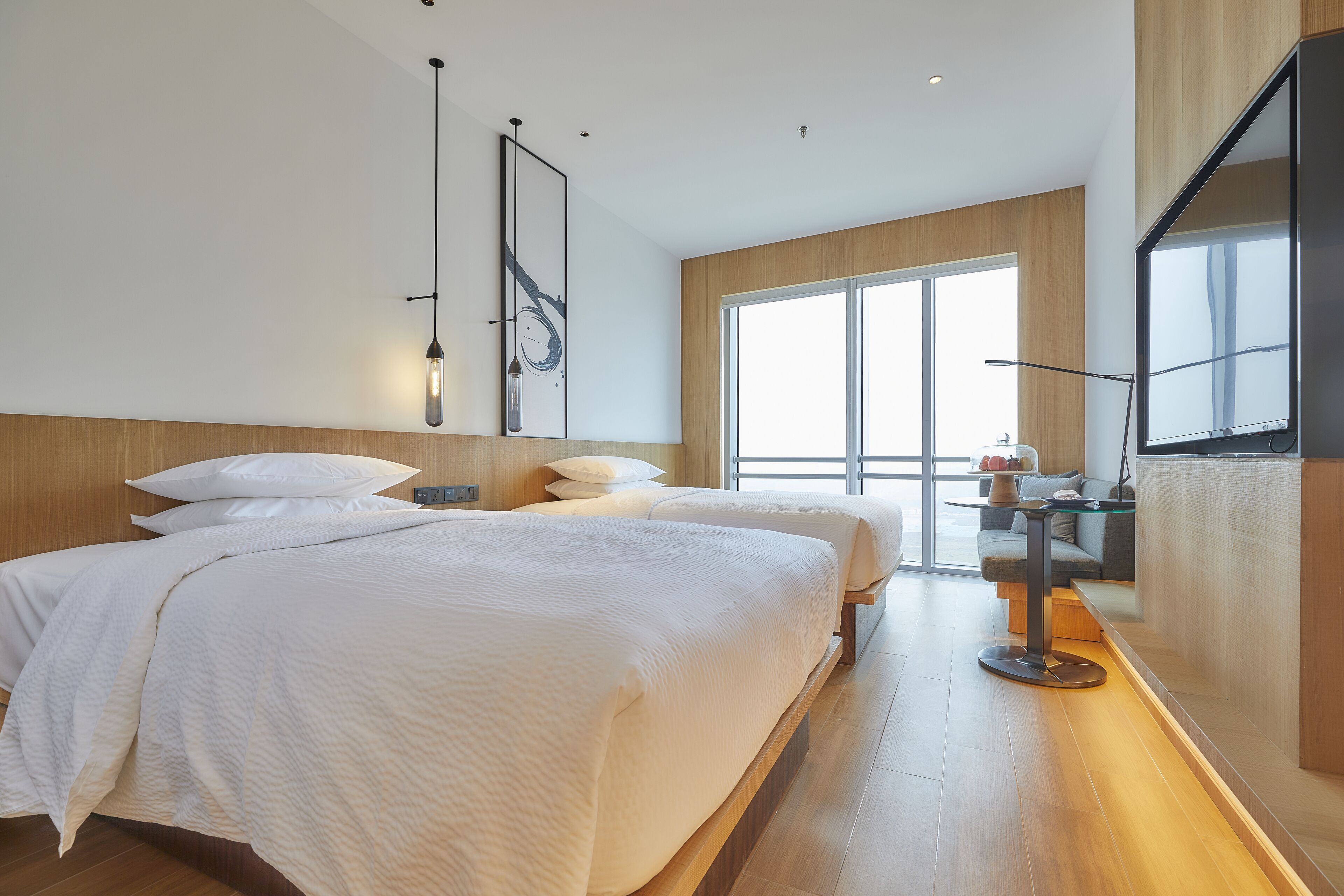 Una habitación de hotel moderna con una cama grande, un escritorio y un ventanal que proporciona luz natural.