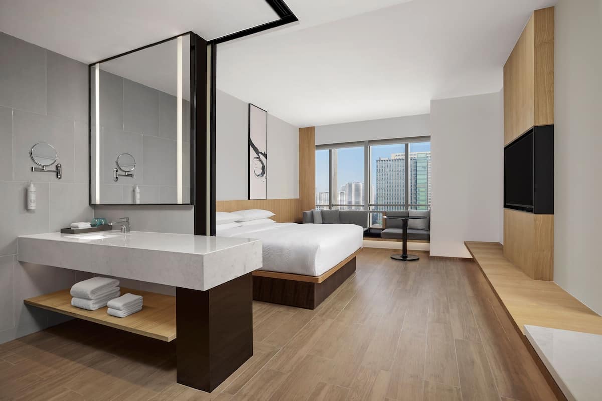 Una habitación de hotel moderna con un espejo grande, una cama, televisor integrado y vistas a la ciudad.