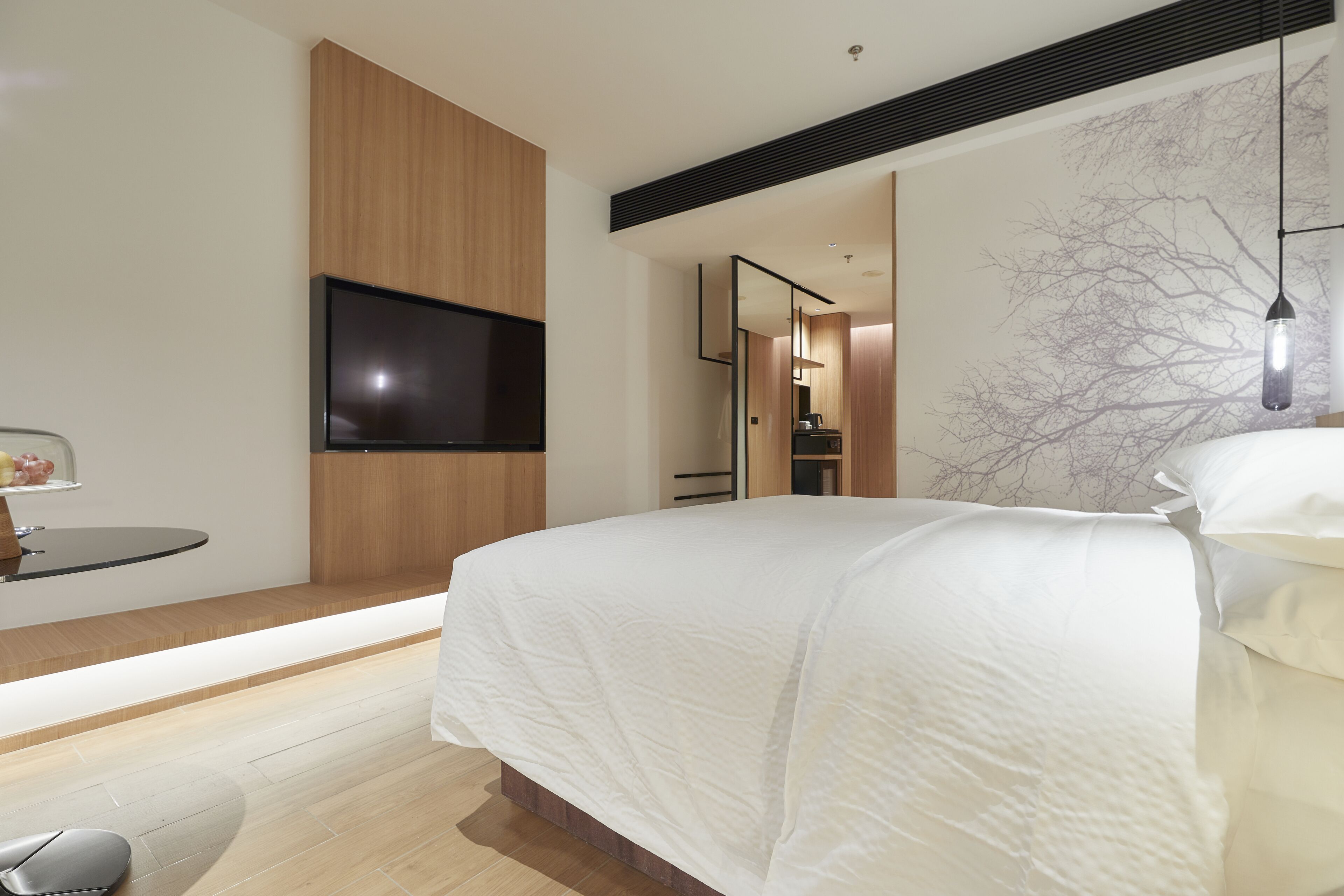 A modern bedroom with a large bed, a flat-screen TV mounted on the wall, and a minimalist design.