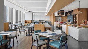 Un restaurante moderno con mesas y sillas altas, una isla central con barra y ventanas amplias que ofrecen luz natural.