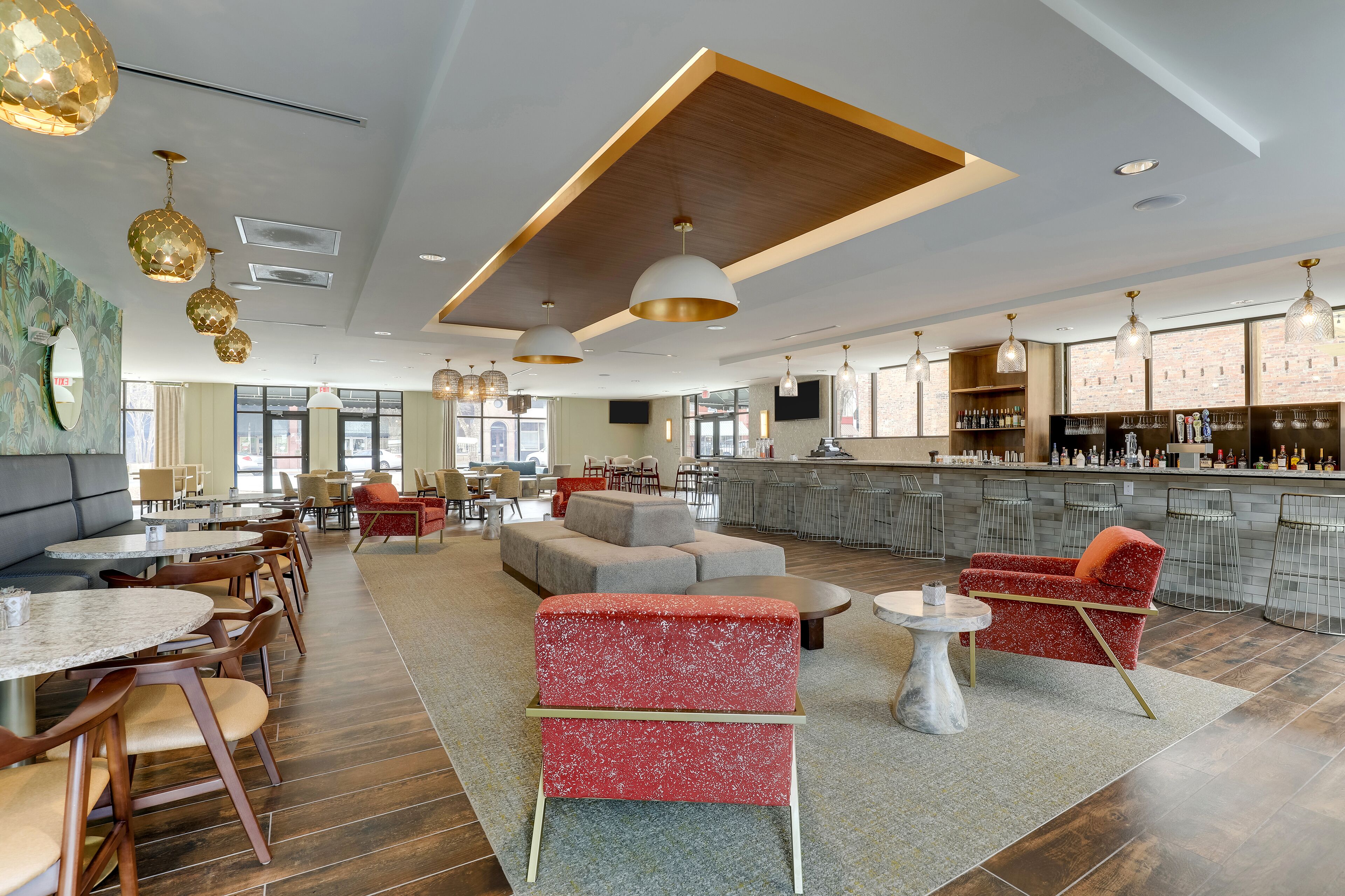 Un hall d’hôtel moderne doté d’un bar, de différents espaces de détente et d’une grande fenêtre laissant entrer la lumière naturelle.