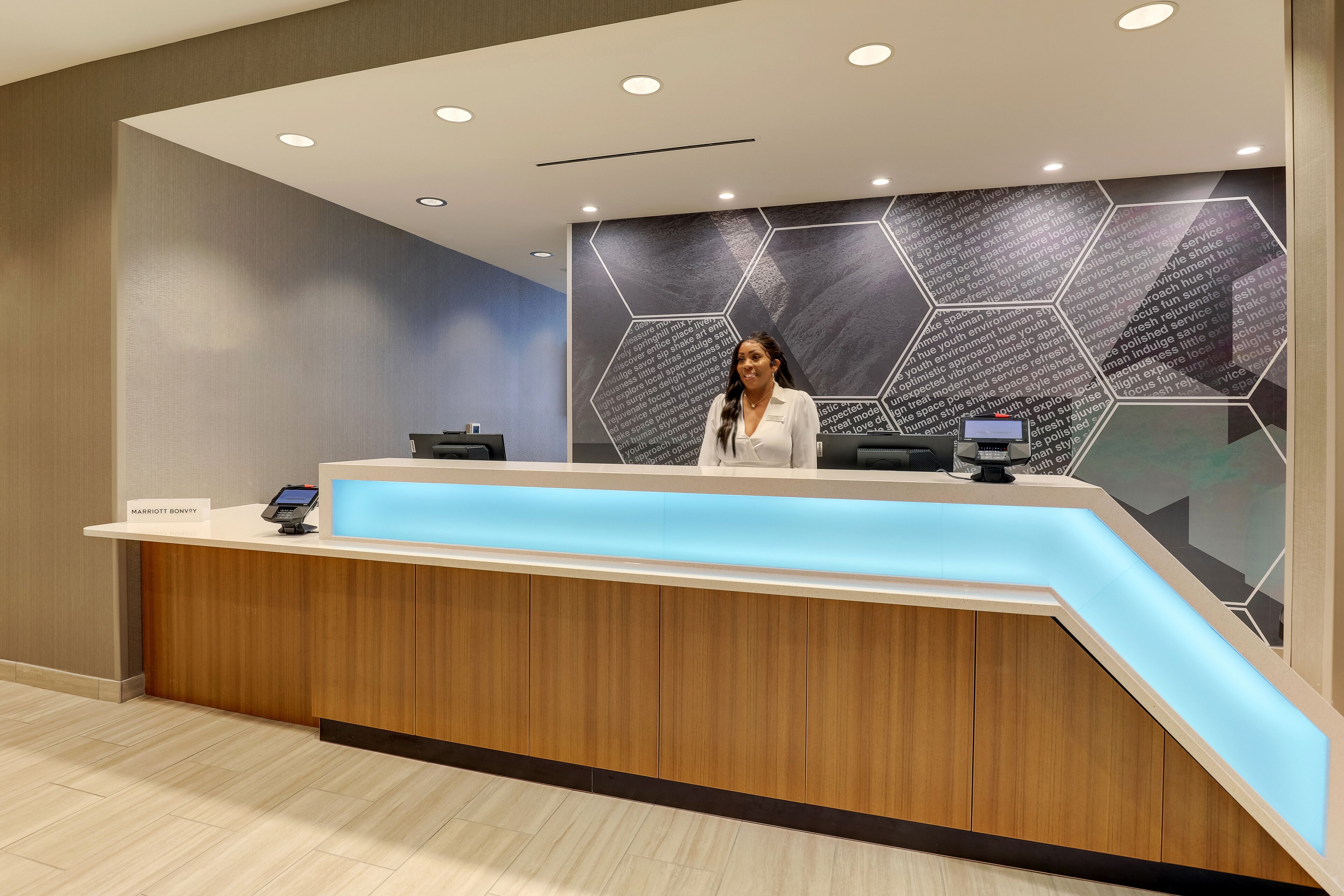 A modern reception desk with a wooden finish and a blue illuminated panel.
