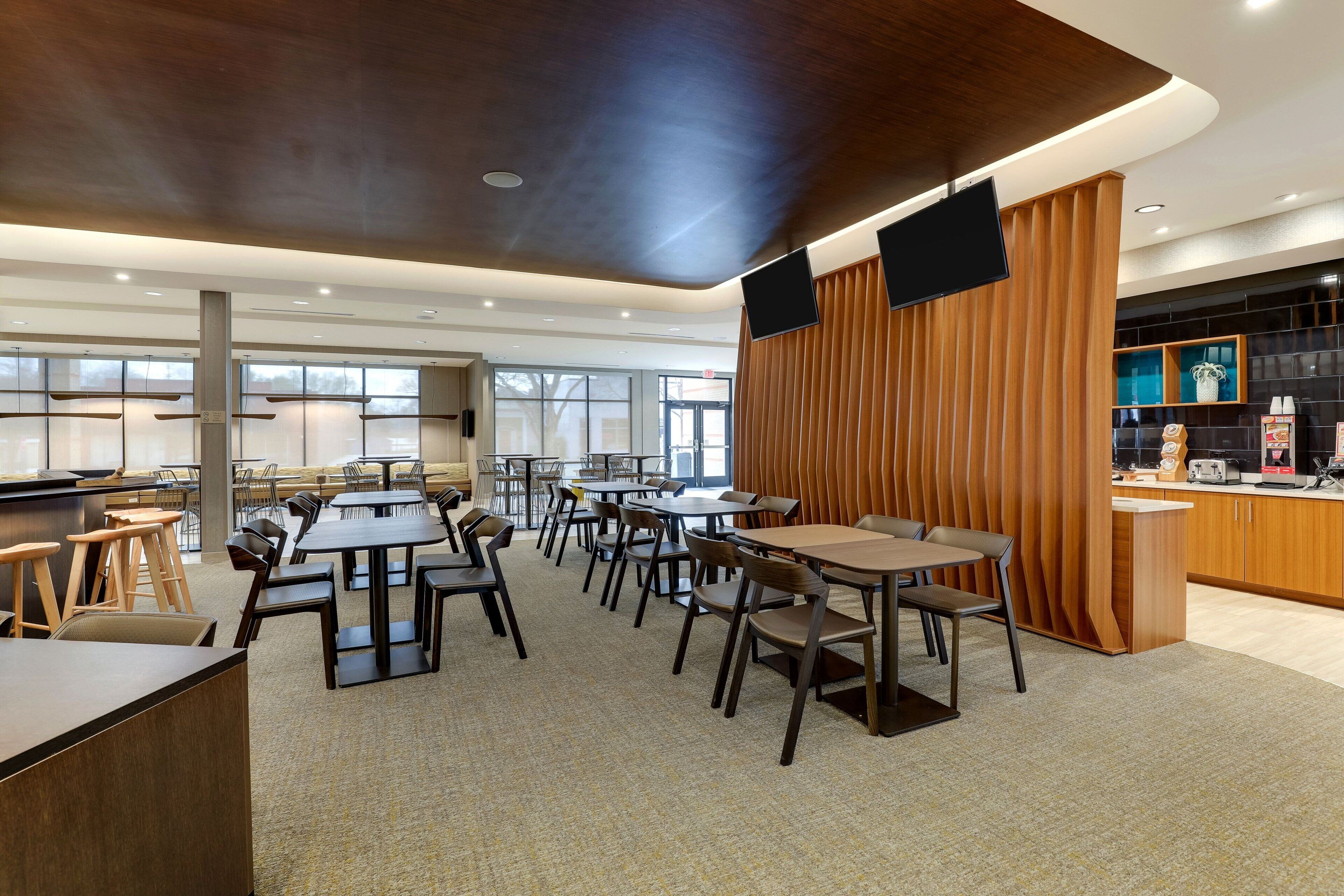 A modern restaurant with multiple tables and chairs, a bar area, and a kitchen visible in the background.