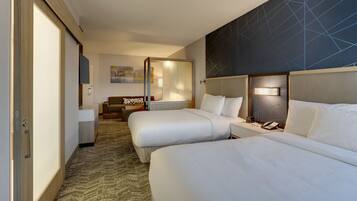 Habitación de hotel con dos camas, un sofá, un escritorio y un televisor de pared.