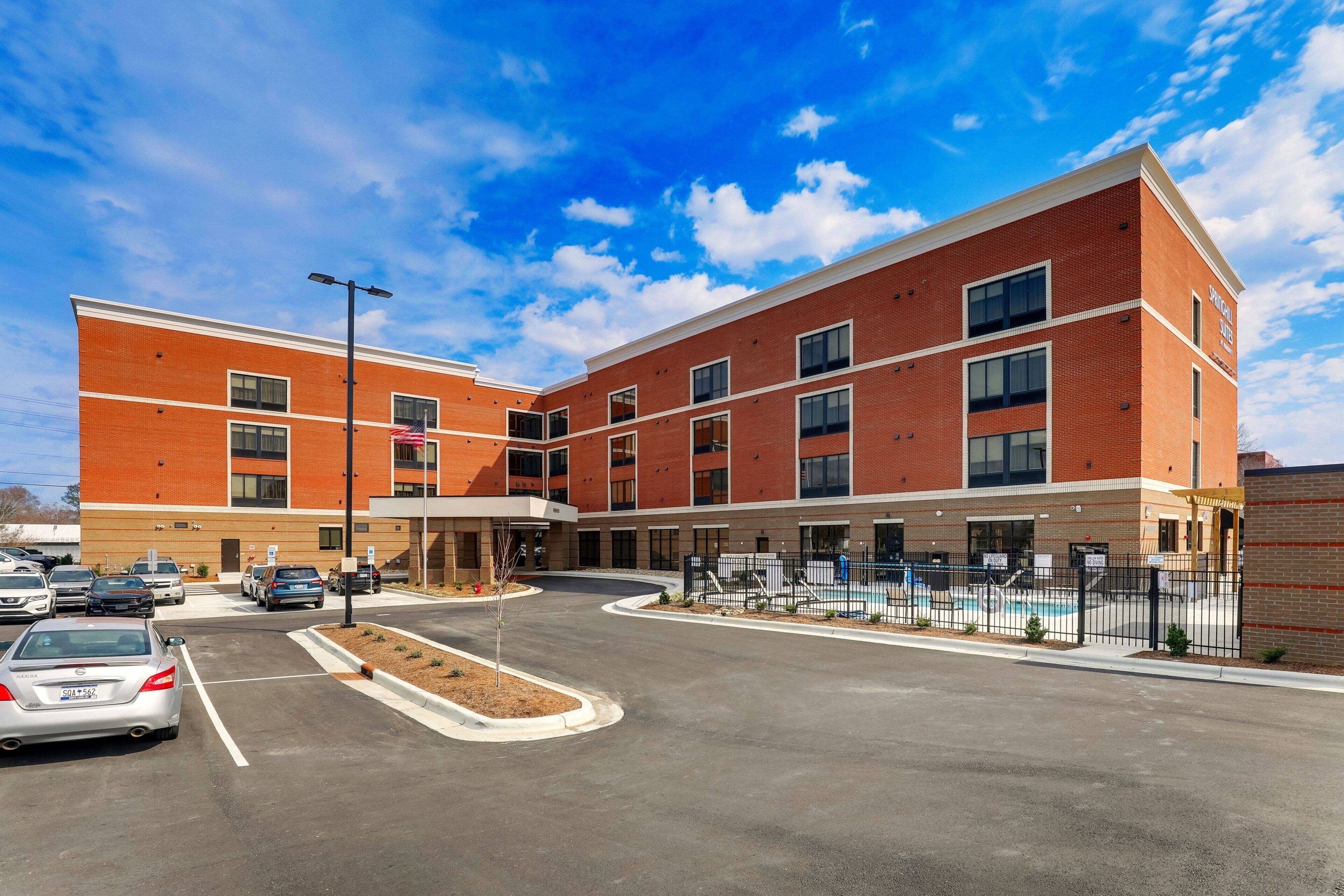 A multi-story hotel with a brick facade, a parking lot, and a swimming pool area.