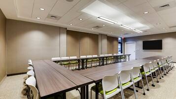 A conference room with a long table, white chairs, and a flat-screen TV on the wall.