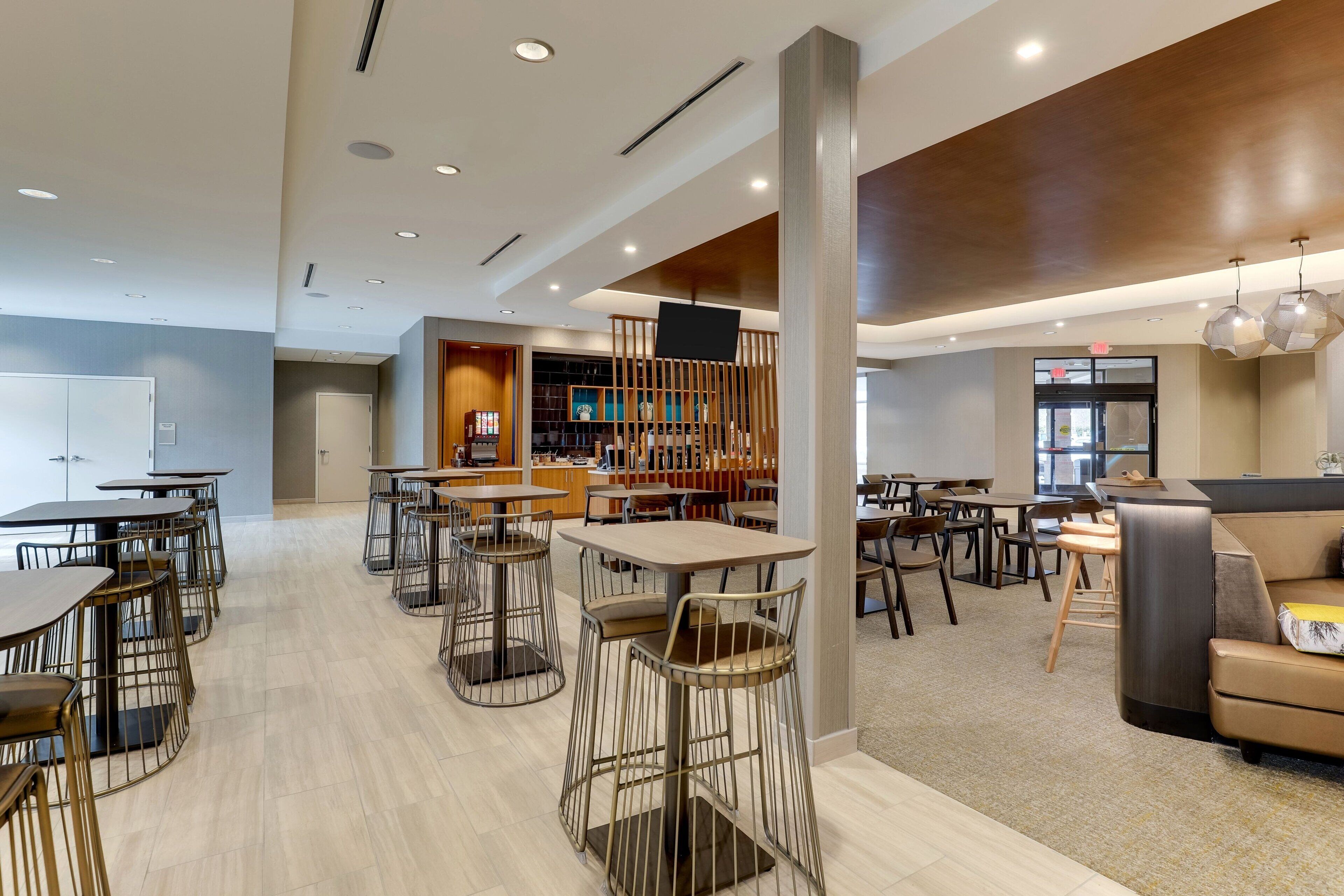 A modern hotel lobby with multiple seating areas, including tables and chairs, a reception desk, and a bar area.
