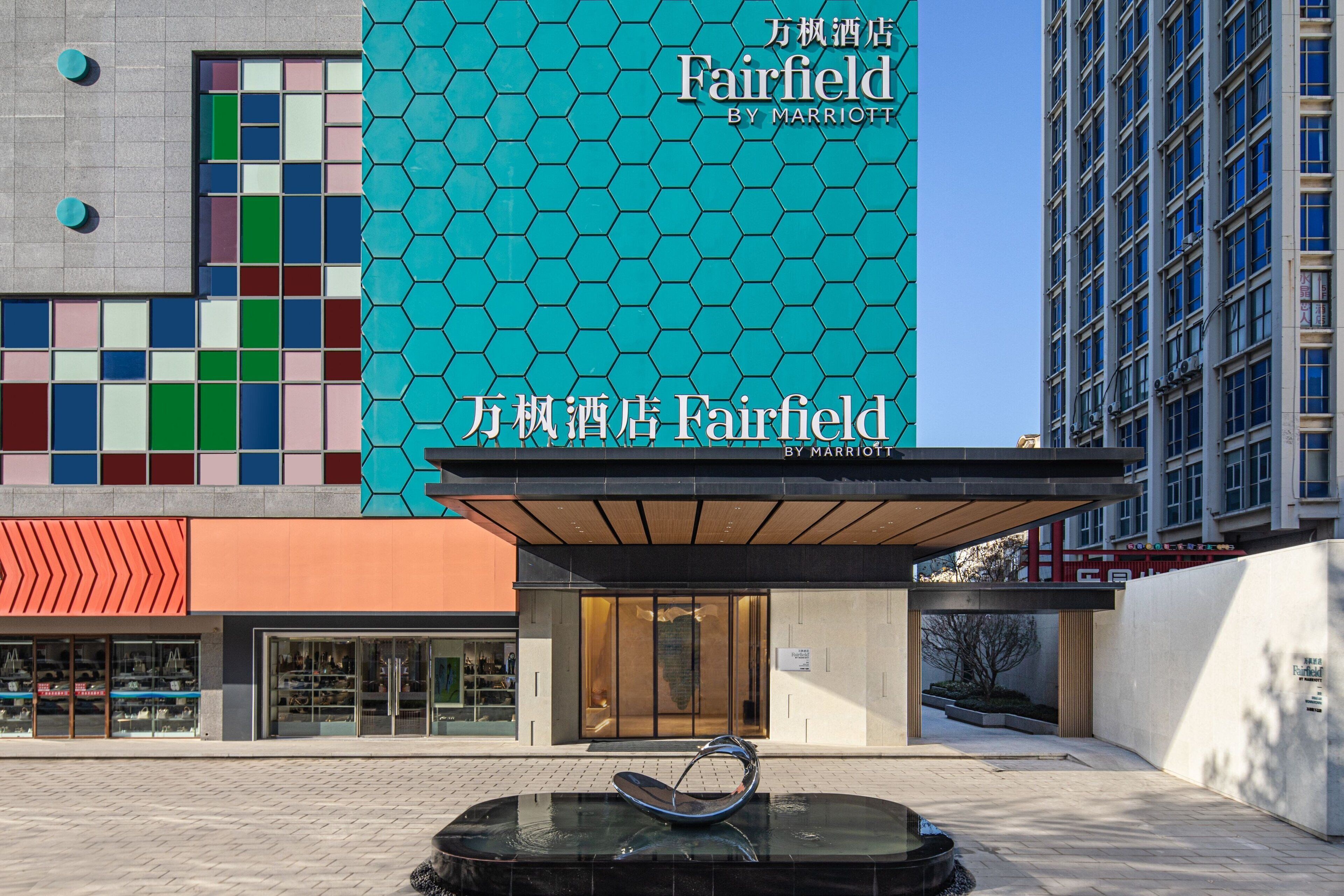 Fachada moderna de un hotel con un letrero destacado de Marriott Fairfield, que presenta un diseño geométrico de azulejos y una entrada despejada.