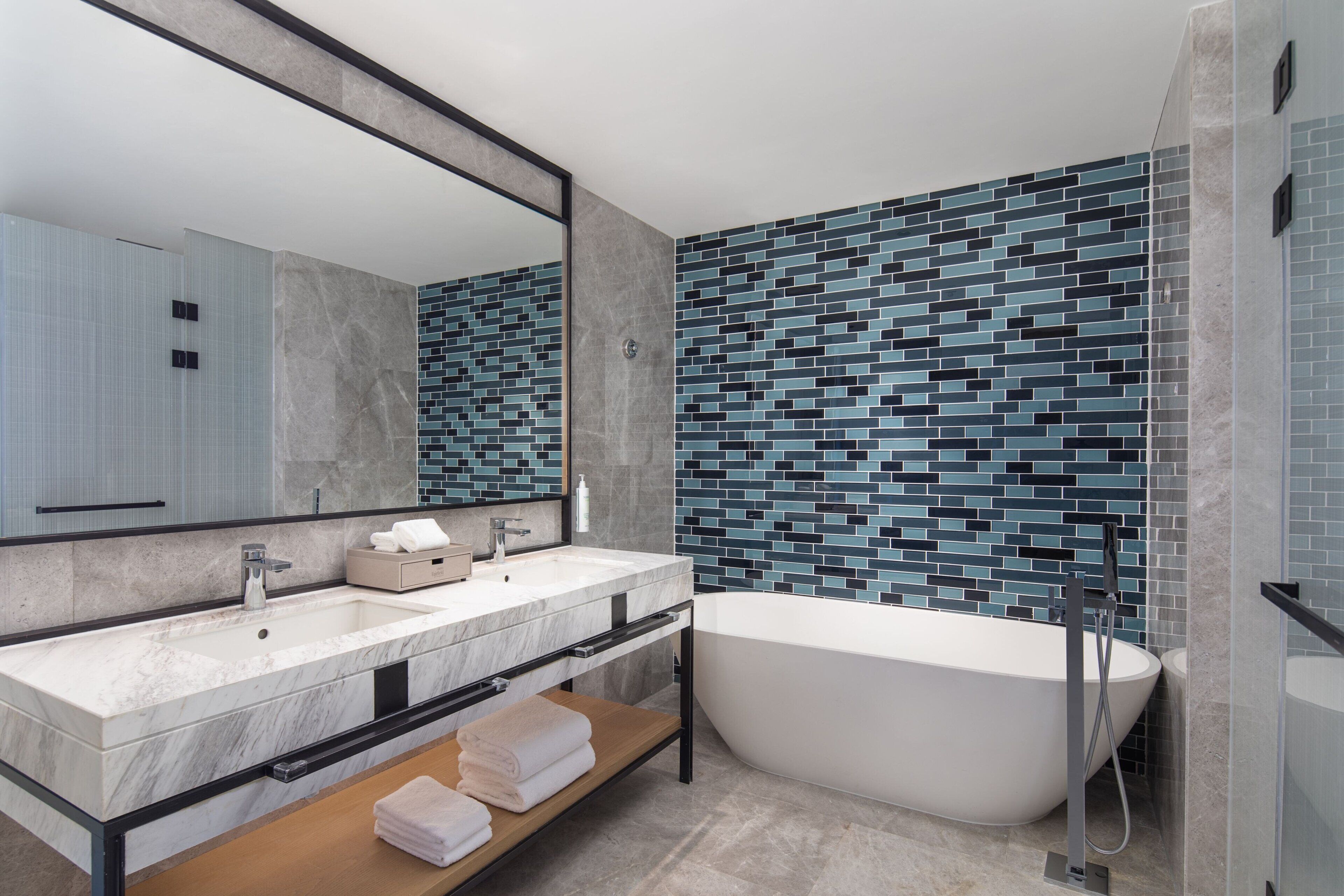 A modern bathroom with a freestanding bathtub, a large mirror, and a tiled backsplash.