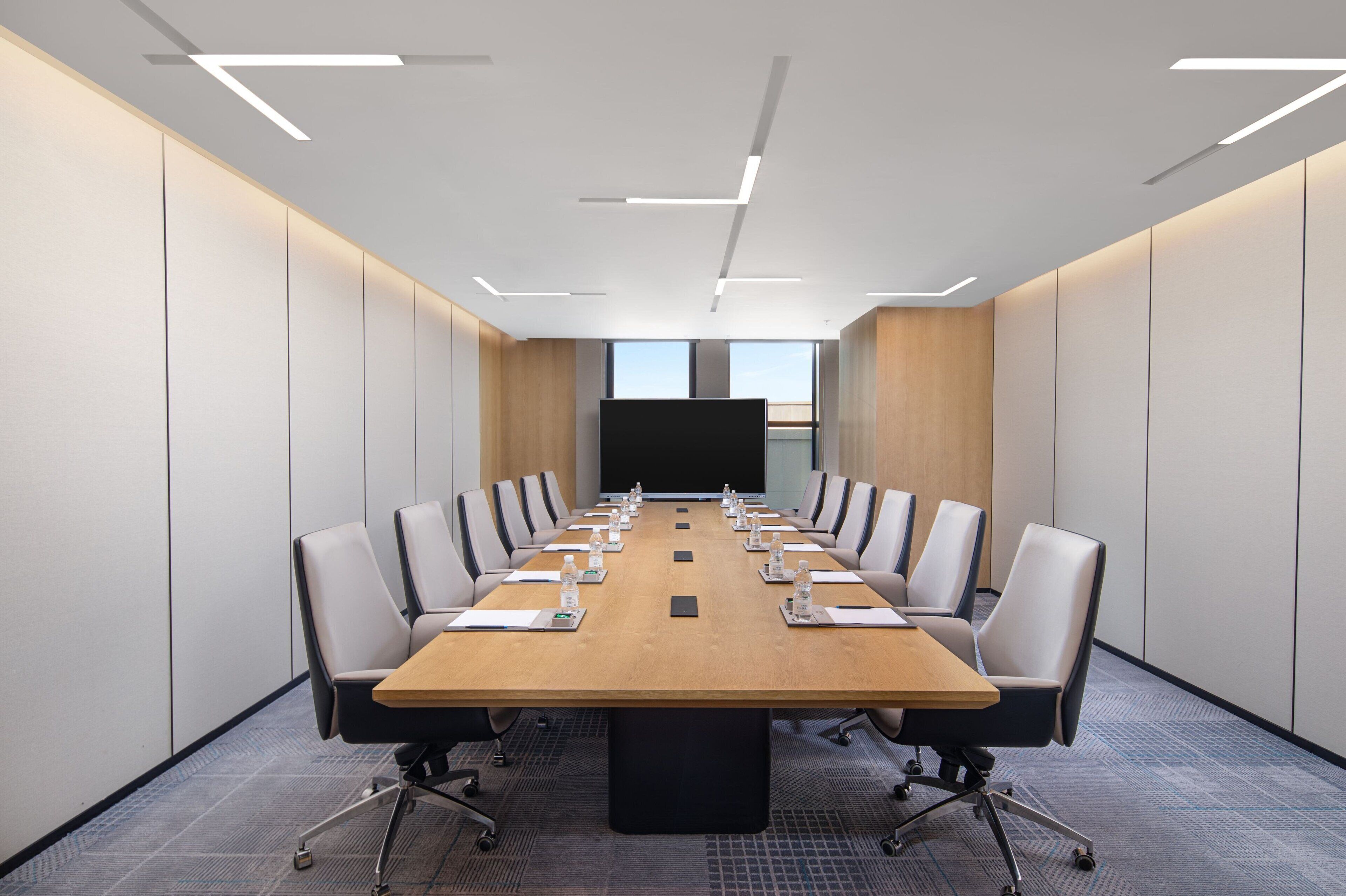 A conference room with a long table, chairs, and a projector screen.