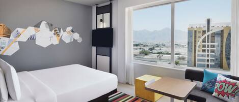 Quarto de hotel moderno com cama, uma mesinha, sofá e uma grande janela com vista para a cidade.