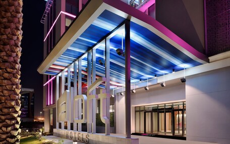 A modern hotel with a distinctive architectural design, featuring a large illuminated sign and a covered outdoor area.