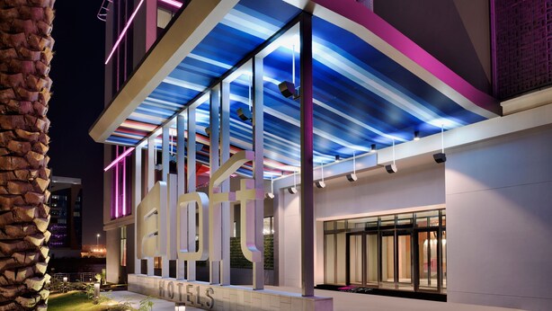 A modern hotel with a distinctive architectural design, featuring a large illuminated sign and a covered outdoor area.