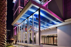 Un hotel moderno con un diseño arquitectónico distintivo, que presenta un gran letrero iluminado y un espacio exterior cubierto.
