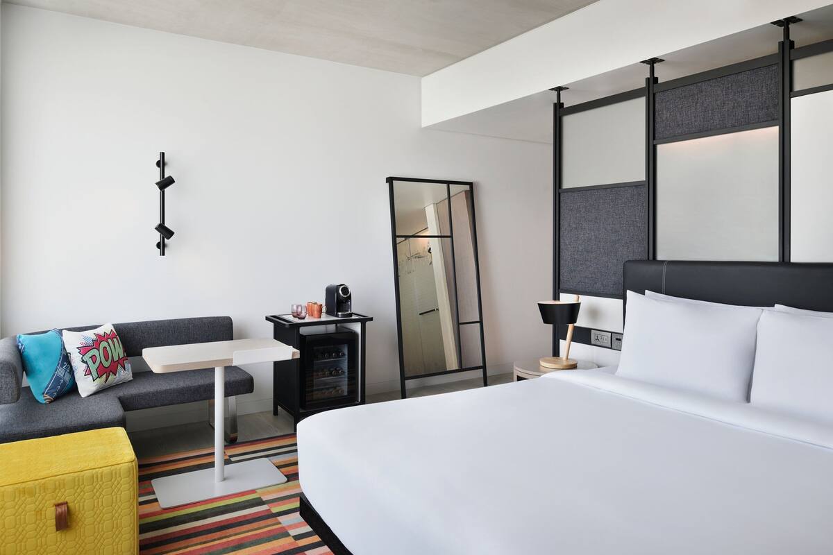 Habitación de hotel con cama, sofá, una mesita, espejo y escritorio con lámpara.