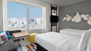 A hotel room with a large window, a bed, a sofa, a small table, and a colorful rug.