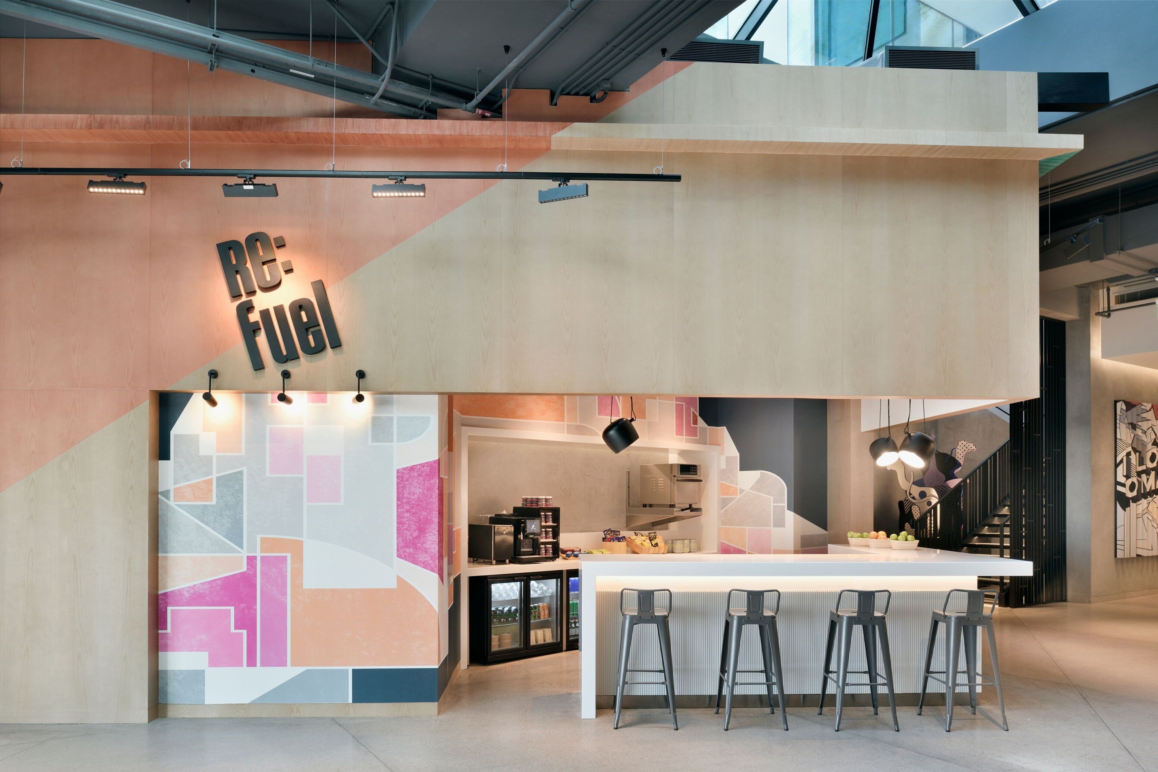 A modern kitchen with a bar area, featuring a geometric wall design and a sign that reads "RE: Fuel".
