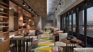 A modern interior with a long, colorful patterned floor, wooden shelving with bowls, and a view of the city through large windows.