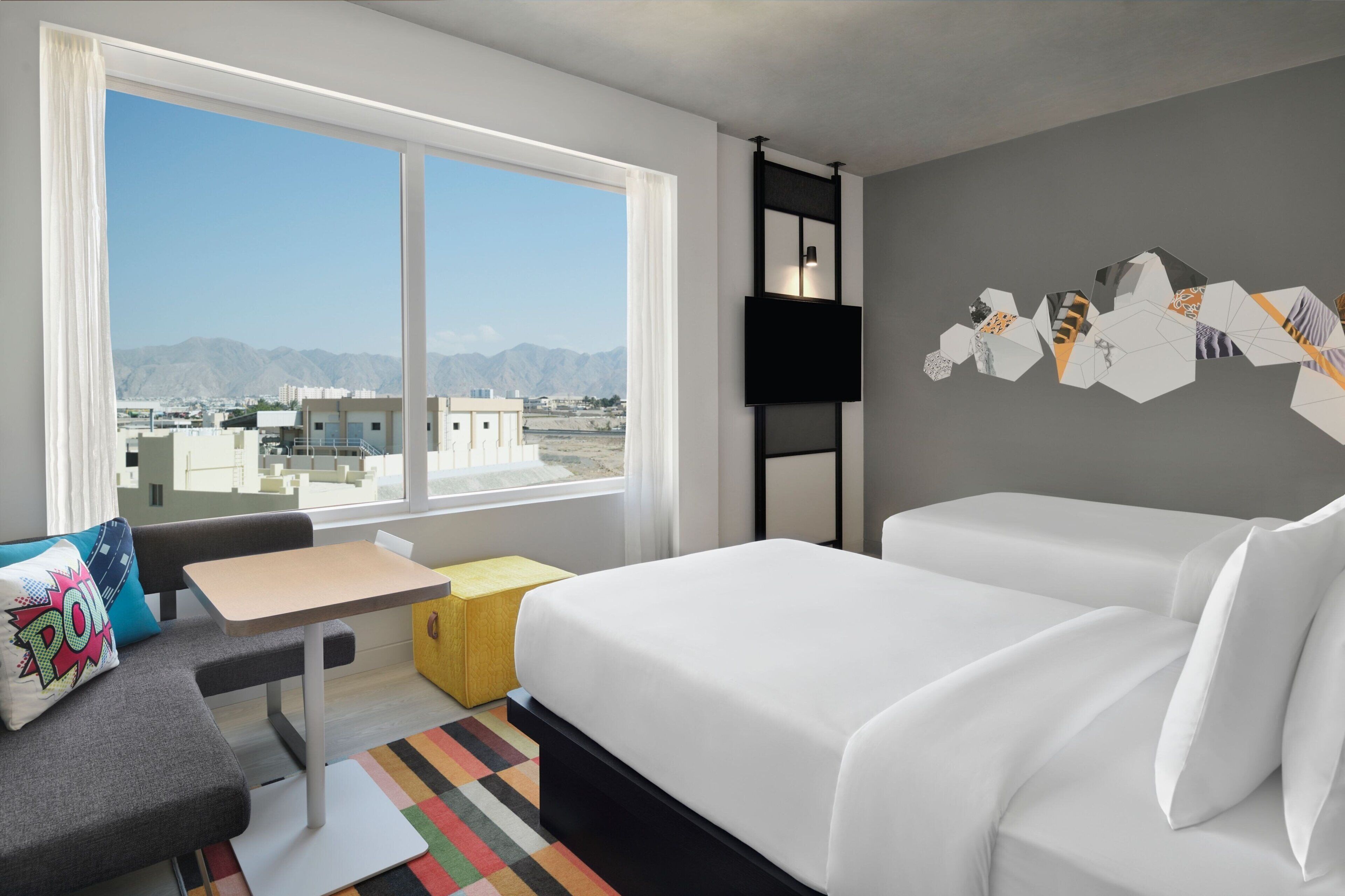 A hotel room with a large window, a bed, a desk, and a chair.