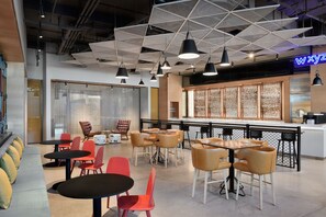 Un café moderne avec des tables noires et rouges, des chaises orange et un plafond au design géométrique.