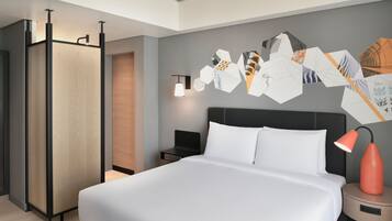 Une chambre d’hôtel moderne avec un grand lit, une table de chevet, une lampe fixée au mur et une œuvre d’art géométrique accrochée au mur.