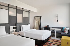 Une chambre d’hôtel avec deux lits, un bureau, un canapé, un miroir et une petite table avec une lampe.