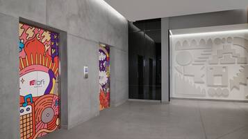 Un hall d’hôtel moderne au design minimaliste, agrémenté d’une fresque murale lumineuse et colorée sur le mur de gauche et d’une œuvre d’art géométrique sur le mur de droite.
