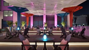 An outdoor lounge area with round tables and chairs, illuminated by ambient lighting.