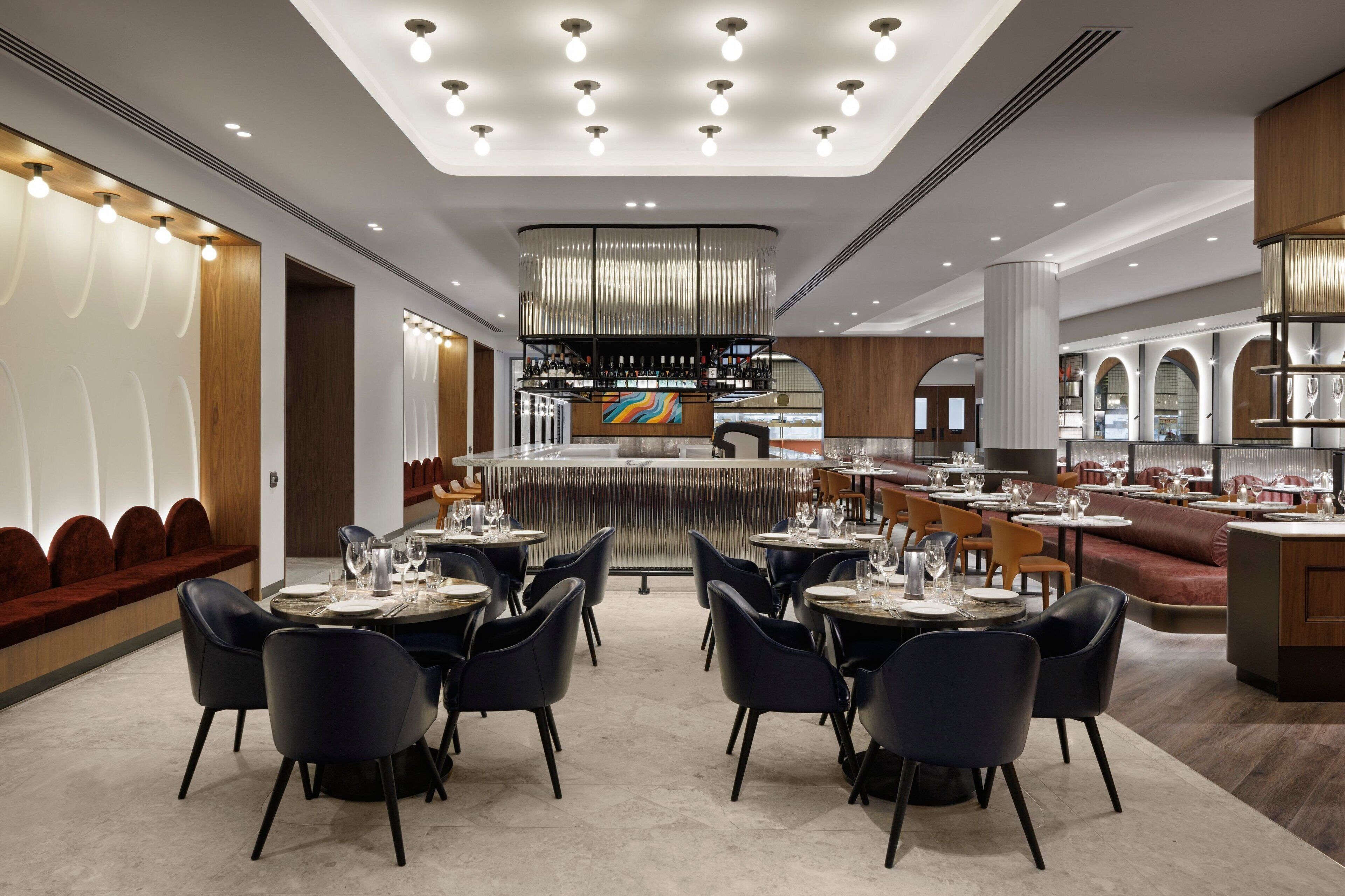 Um restaurante moderno com um bar central, diversas áreas de estar e uma variedade de mesas e cadeiras.
