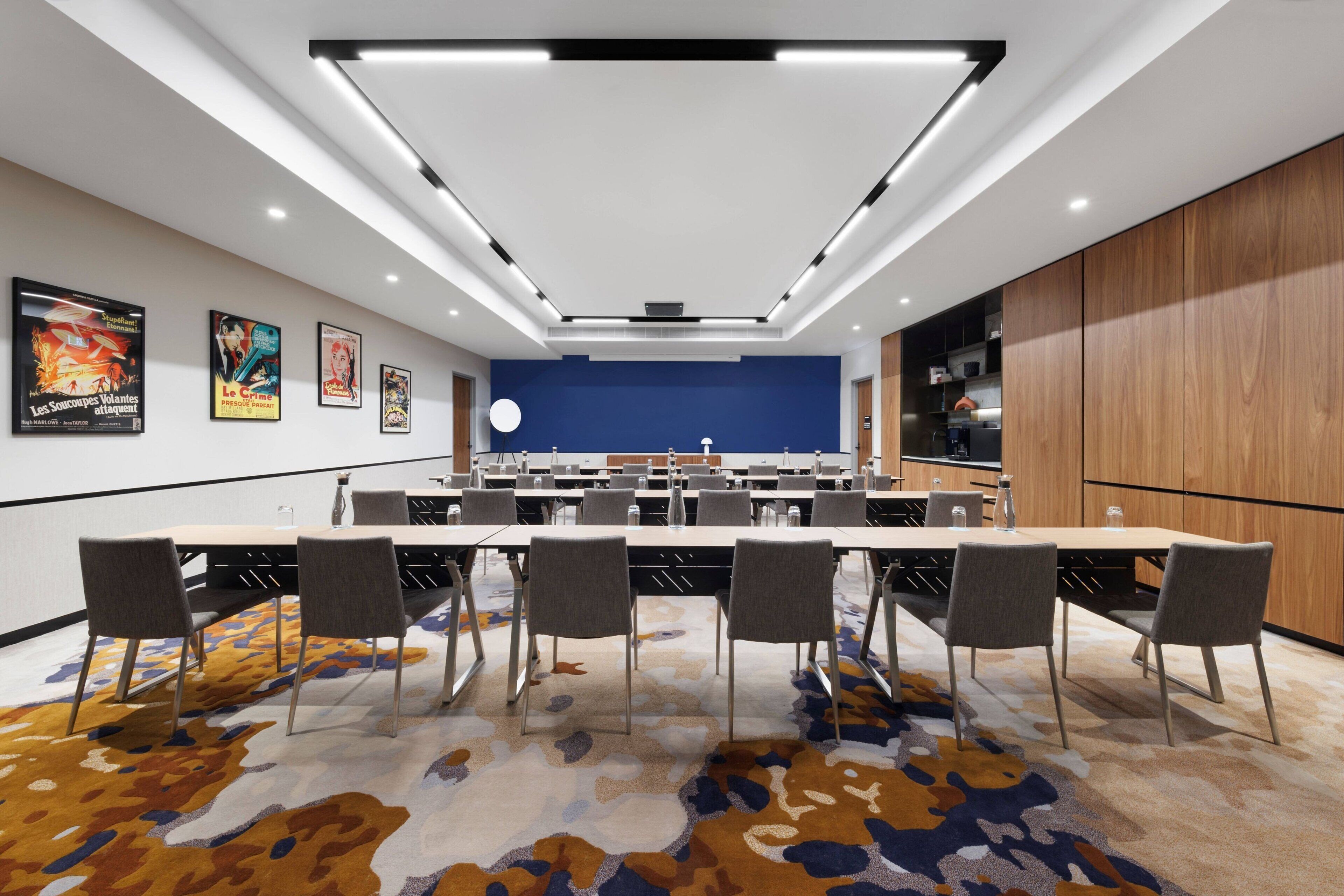 Un salón de conferencias con una larga mesa, sillas y una pared azul decorativa.