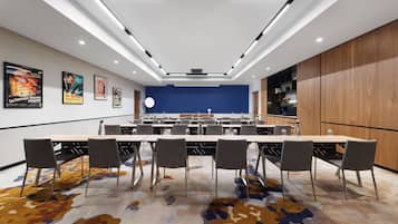 Un salón de conferencias con una larga mesa, sillas y una pared azul decorativa.