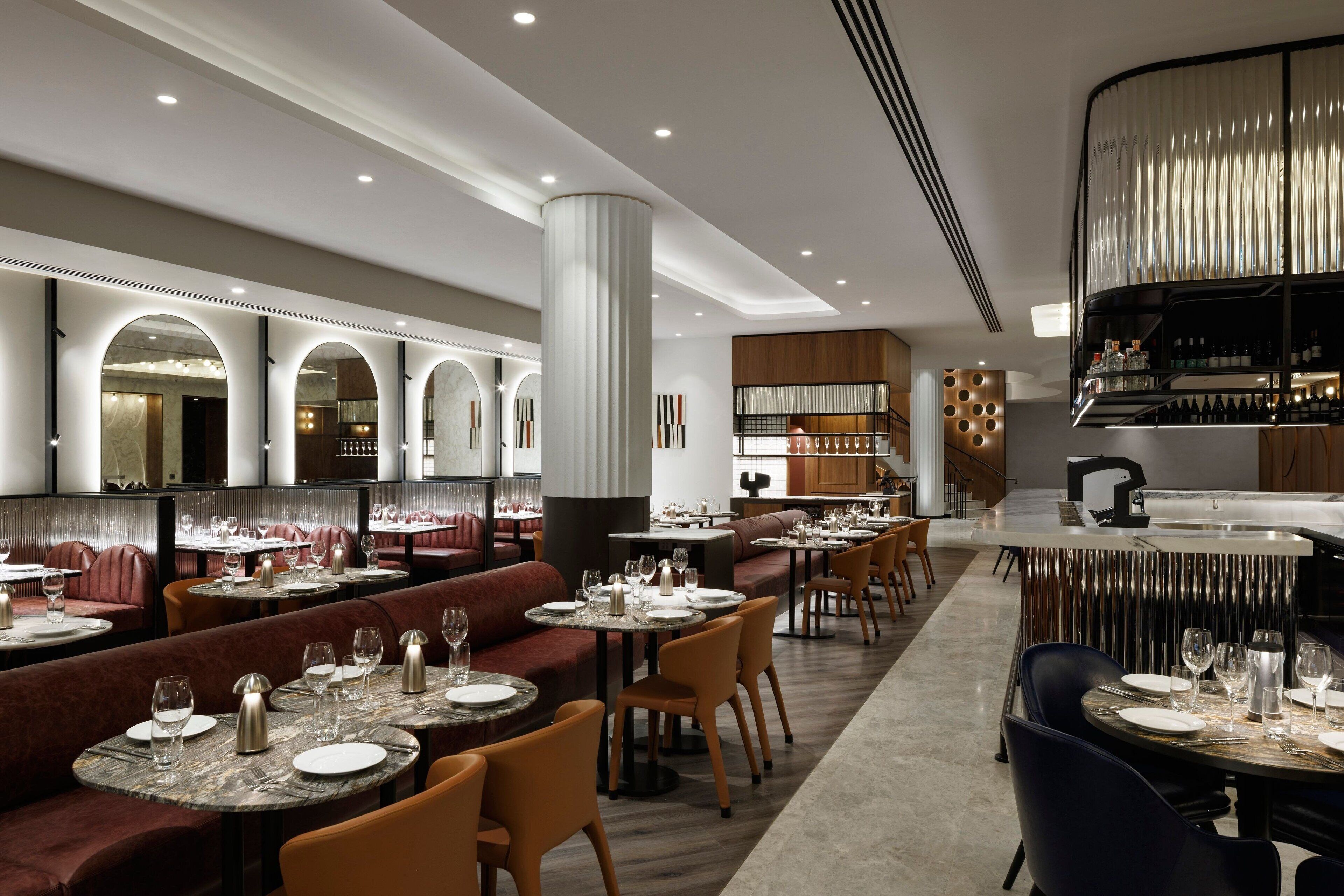 A modern restaurant with round tables, cushioned seating, and a bar area.