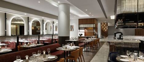 A modern restaurant with round tables, cushioned seating, and a bar area.