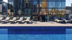 A modern hotel with a reflective glass facade, a rooftop pool, and lounge chairs. - Le Méridien Melbourne (Melbourne)