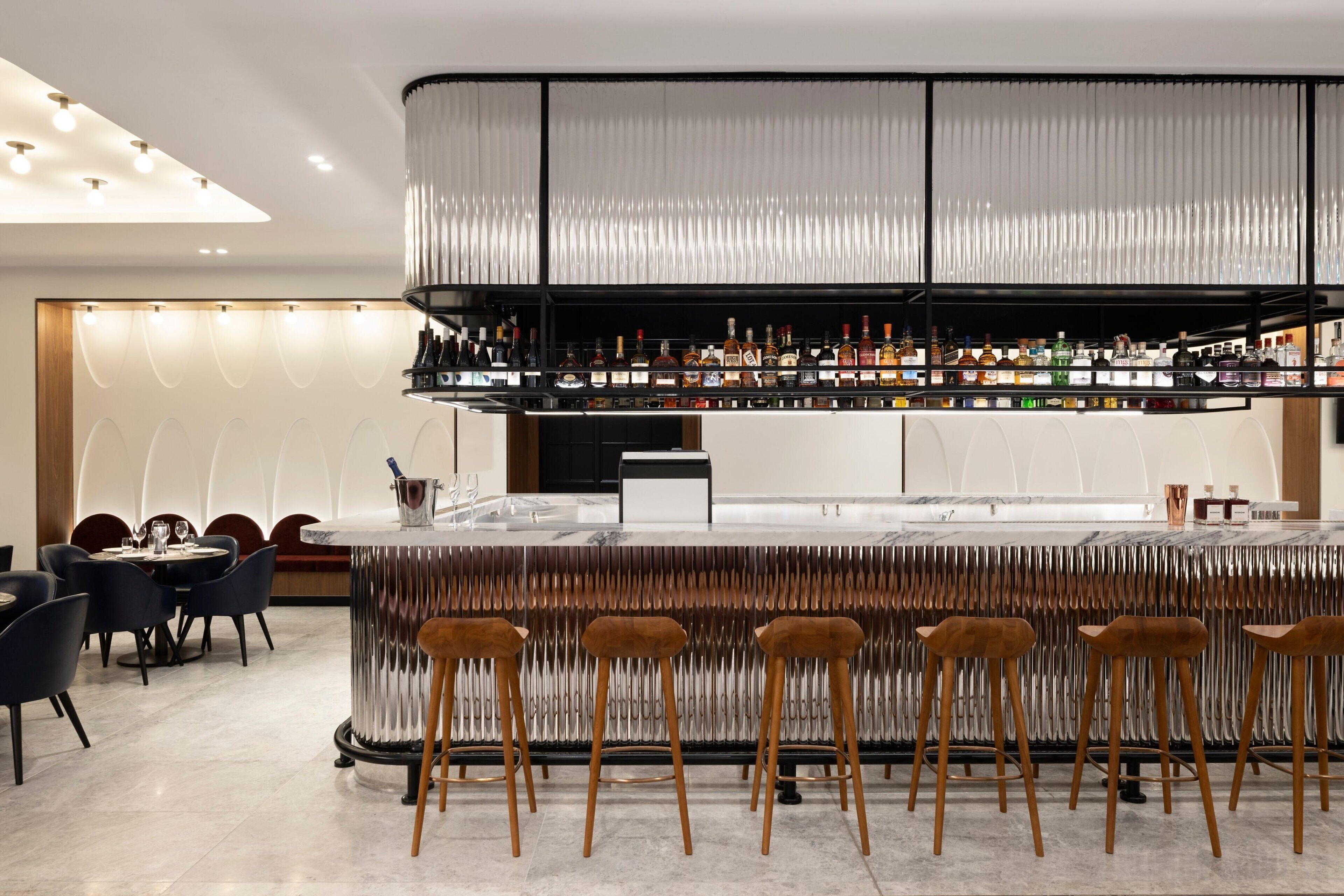 A modern bar area with a high bar counter, multiple stools, and a variety of bottles.