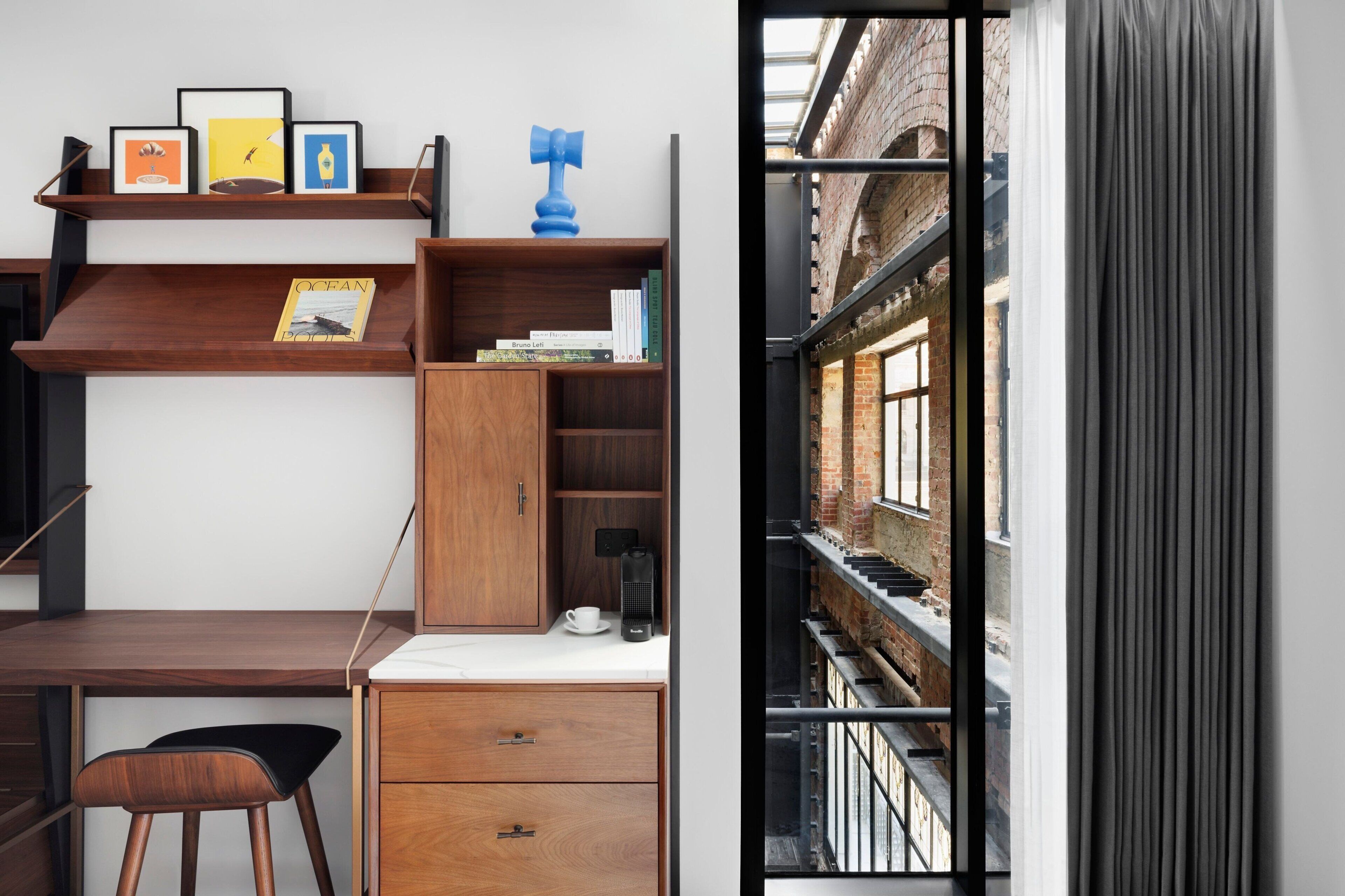 A modern workspace with a wooden desk, shelves with framed pictures, and a view of an urban street through a window.