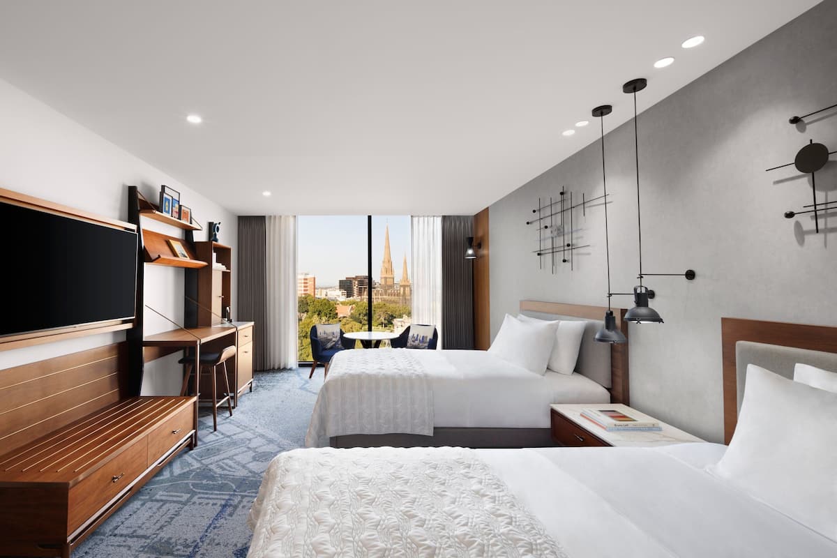 A hotel room with a large bed, a desk with a chair, a TV, and a view of the city.