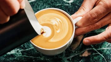 Een detailfoto van handen die een kop koffie met een schuimige laag roeren met een lepel.