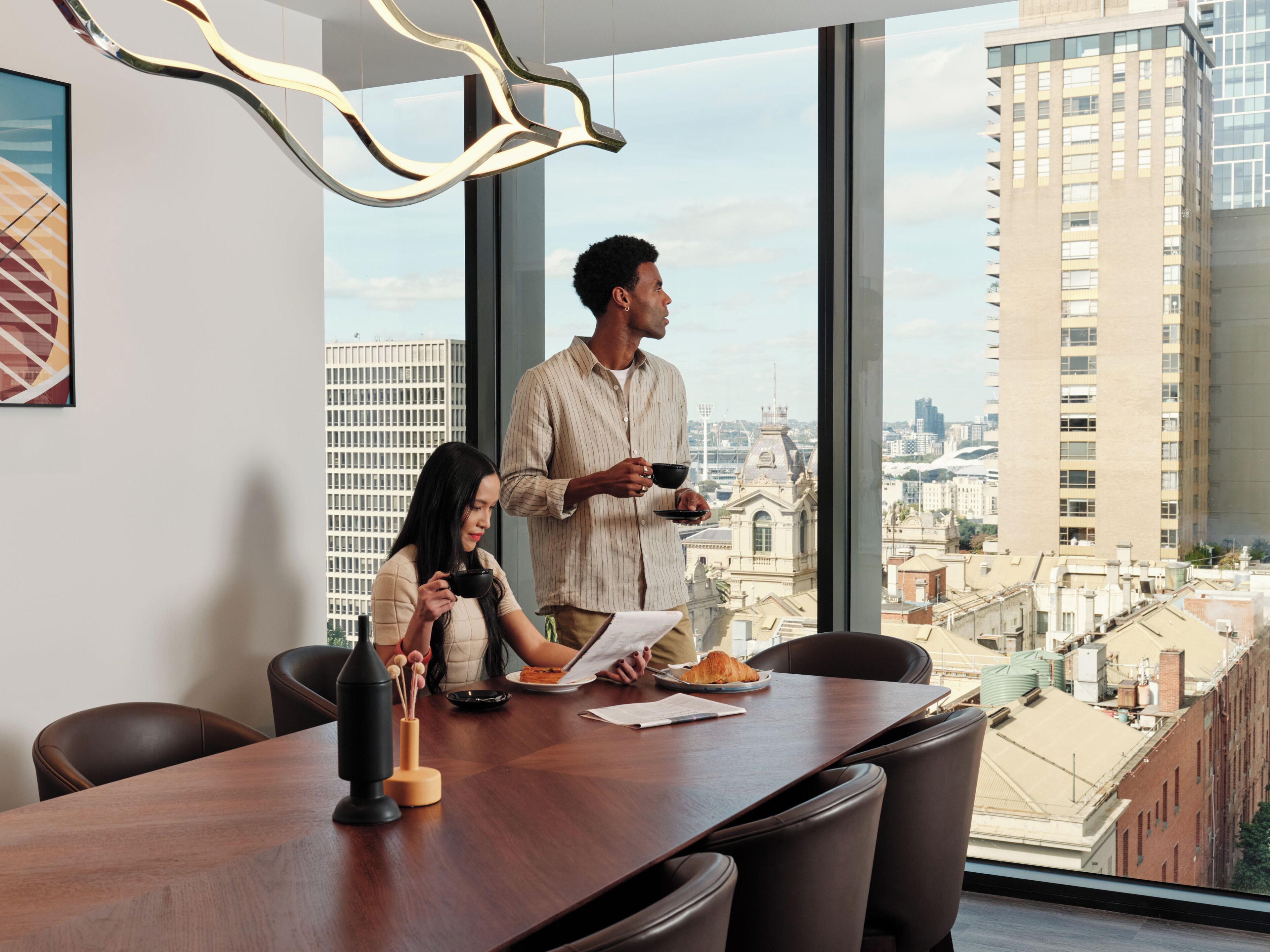 A modern office space with a large table, chairs, and a view of the cityscape through large windows.