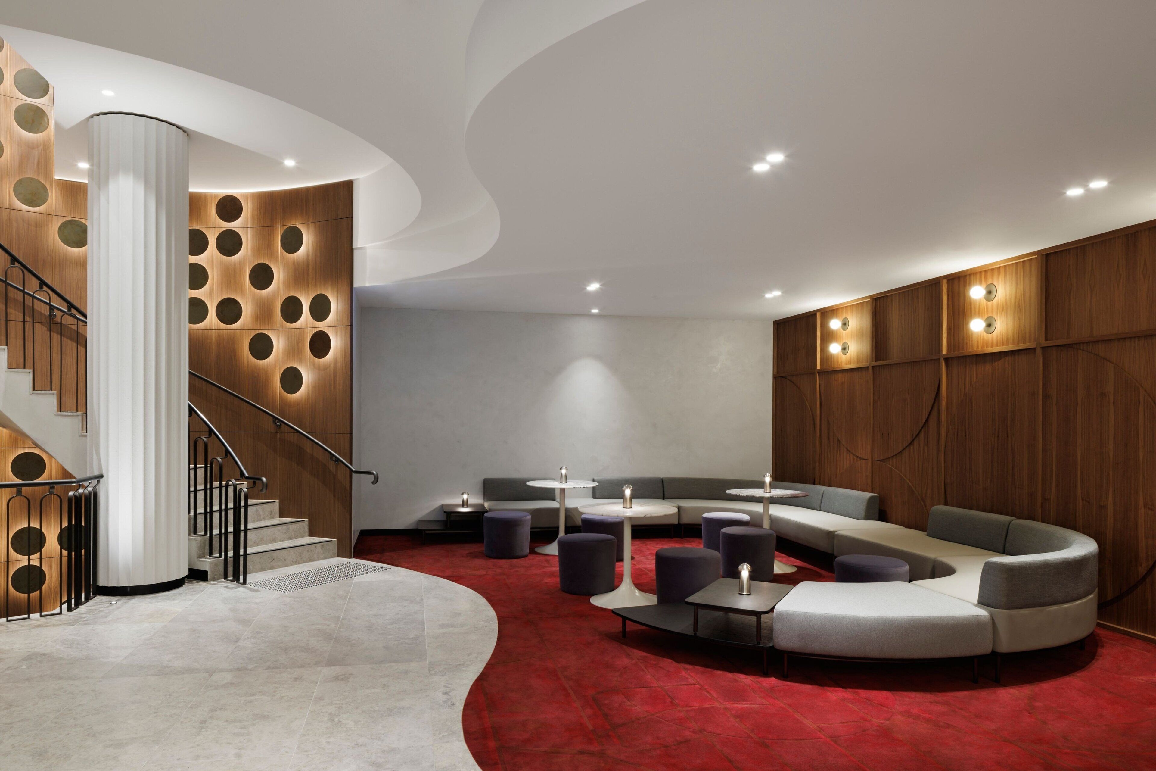 A modern lobby with a curved staircase, seating areas, and a red carpet.
