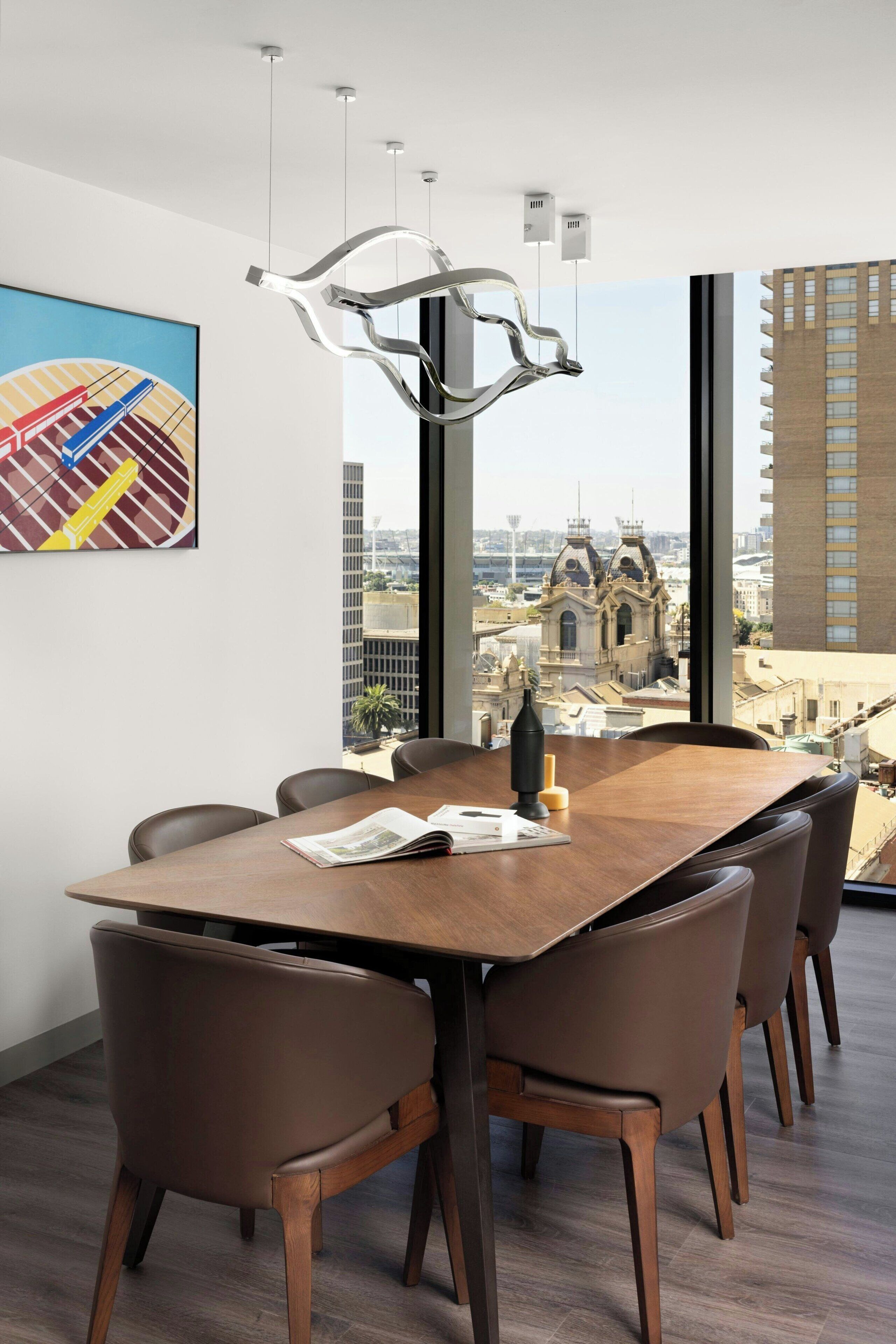 Ein moderner Konferenzraum mit großem Tisch, Ledersesseln und Blick auf eine Stadtlandschaft durch große Fenster.