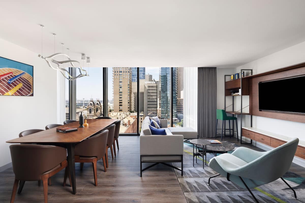 A modern living room with a dining area, a large TV, and a city view.