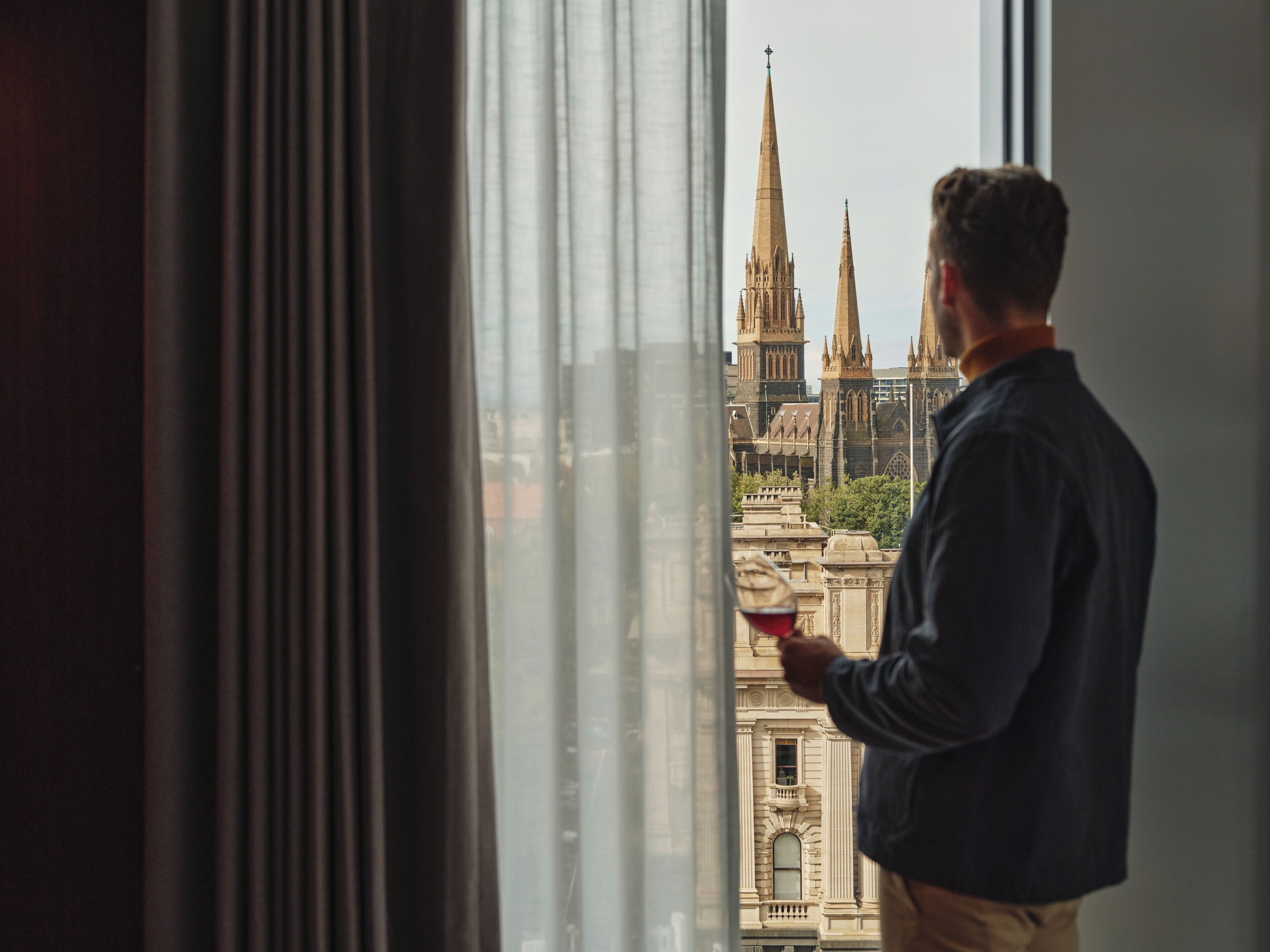 A person standing by a window with a view of a historic building with spires.