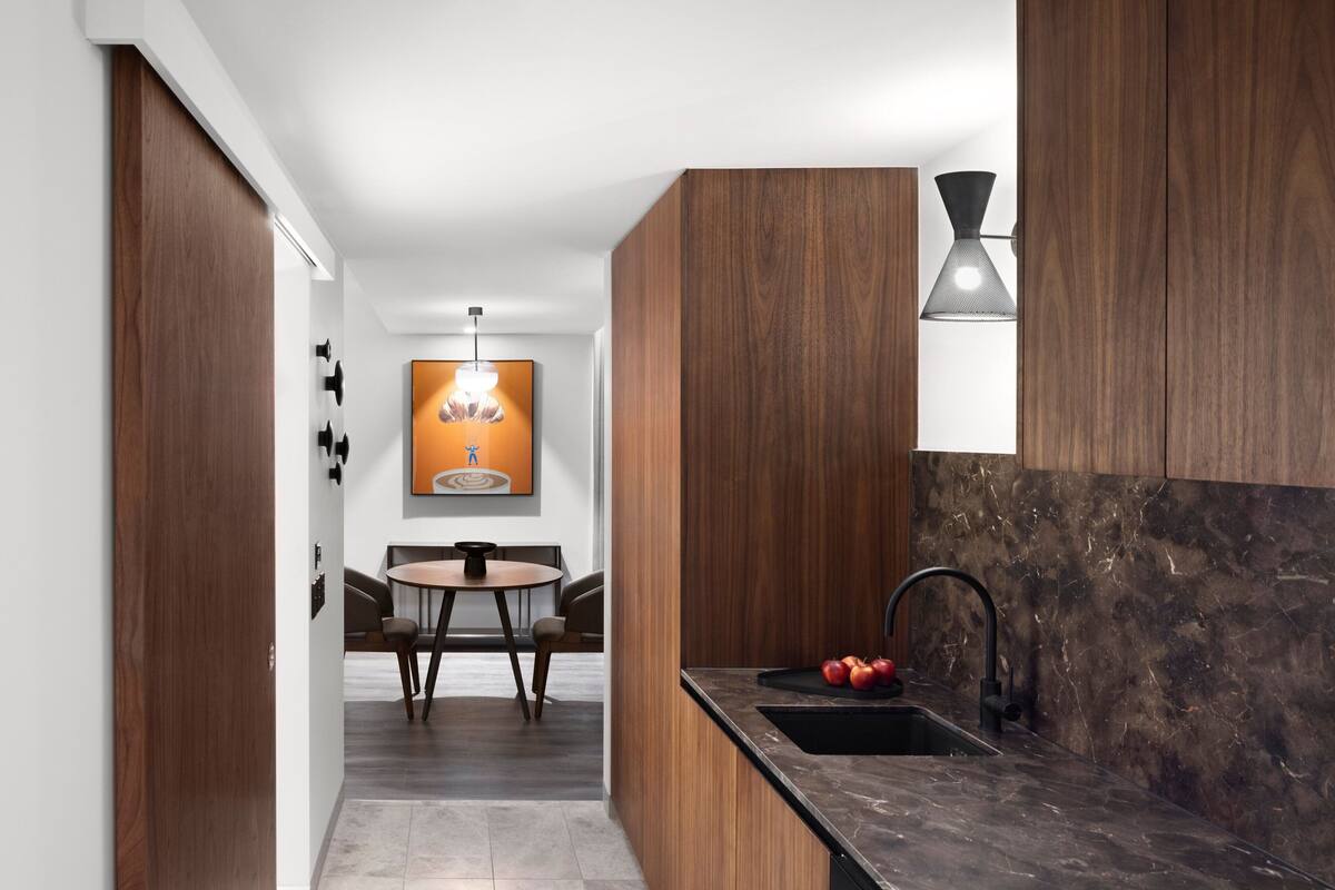 A modern kitchen with dark wood cabinets, a black countertop, and a single sink.