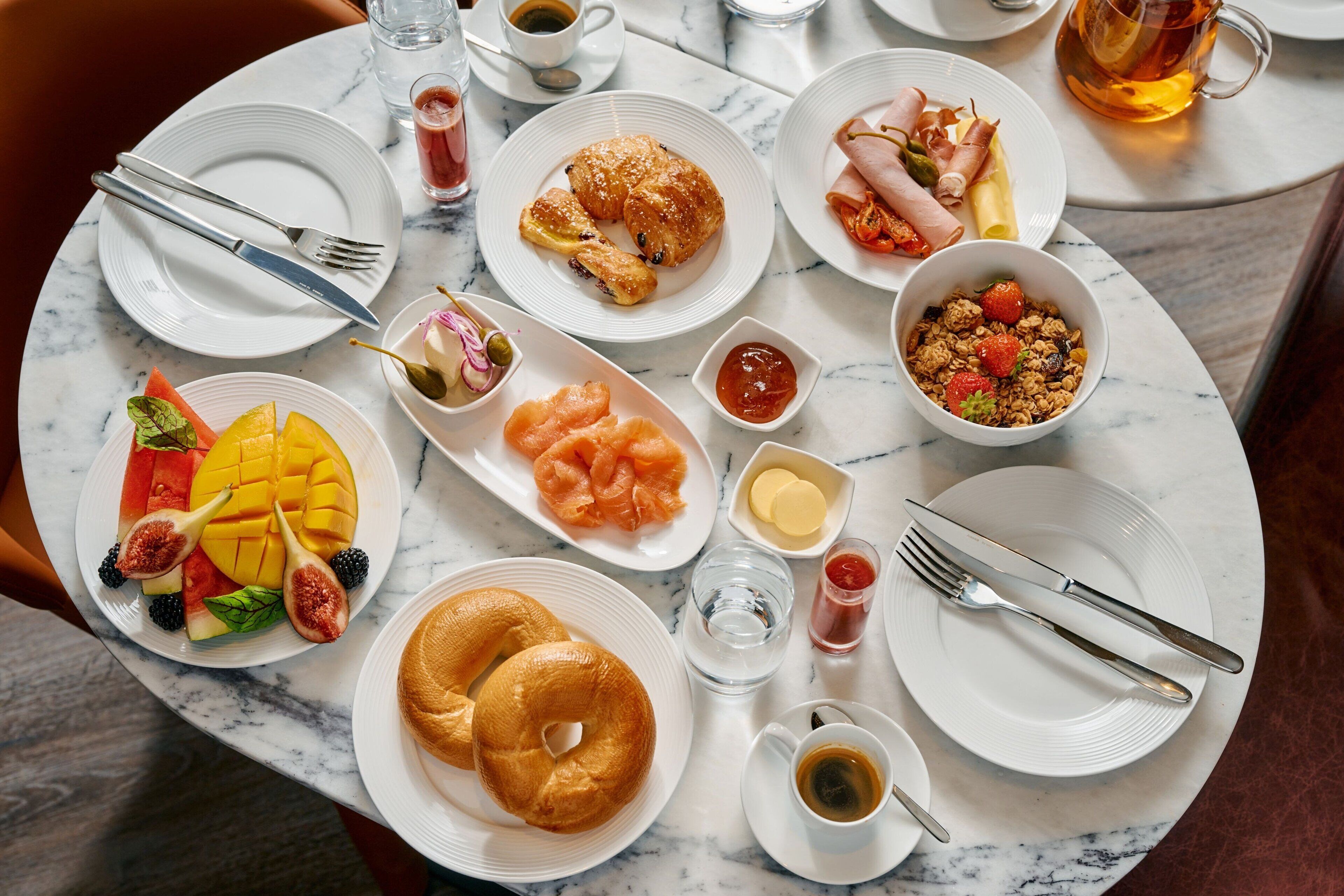 Une table de petit-déjeuner avec divers aliments, assiettes, couverts et verres.