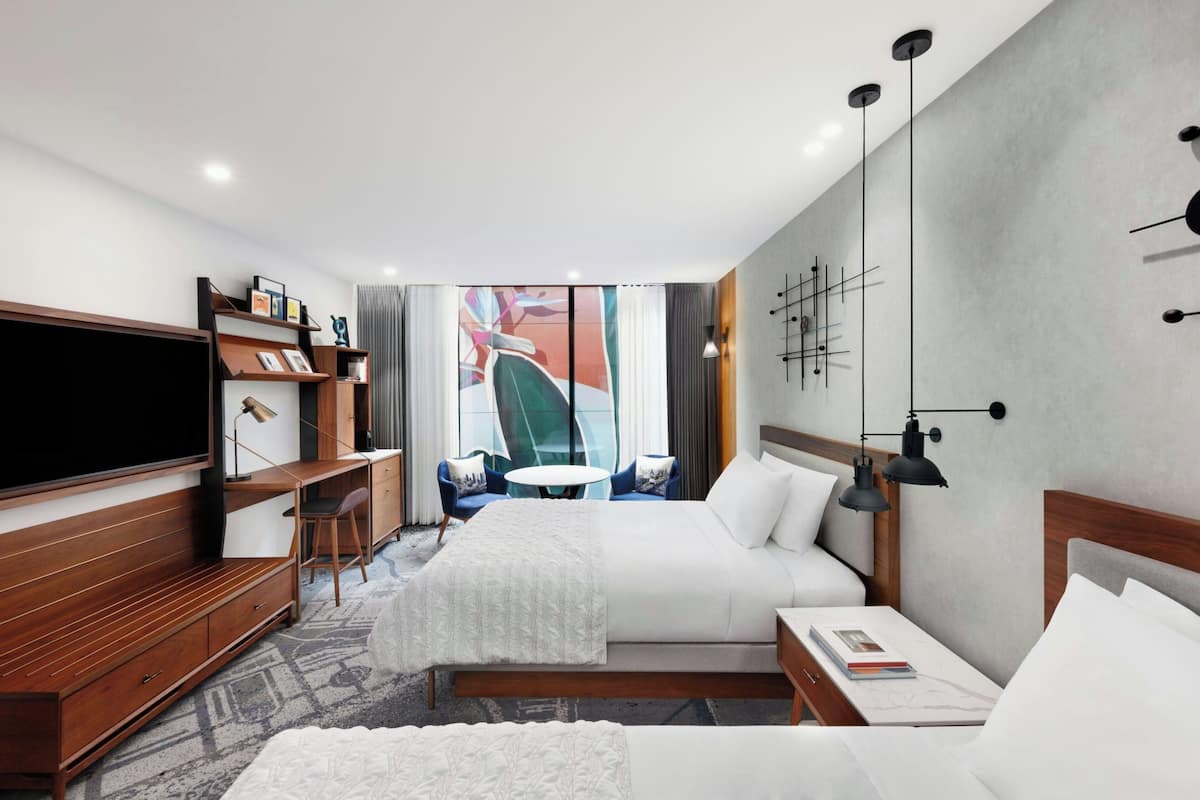 A modern hotel room with a large flat-screen TV, a wooden desk, a comfortable bed, and a small round table.