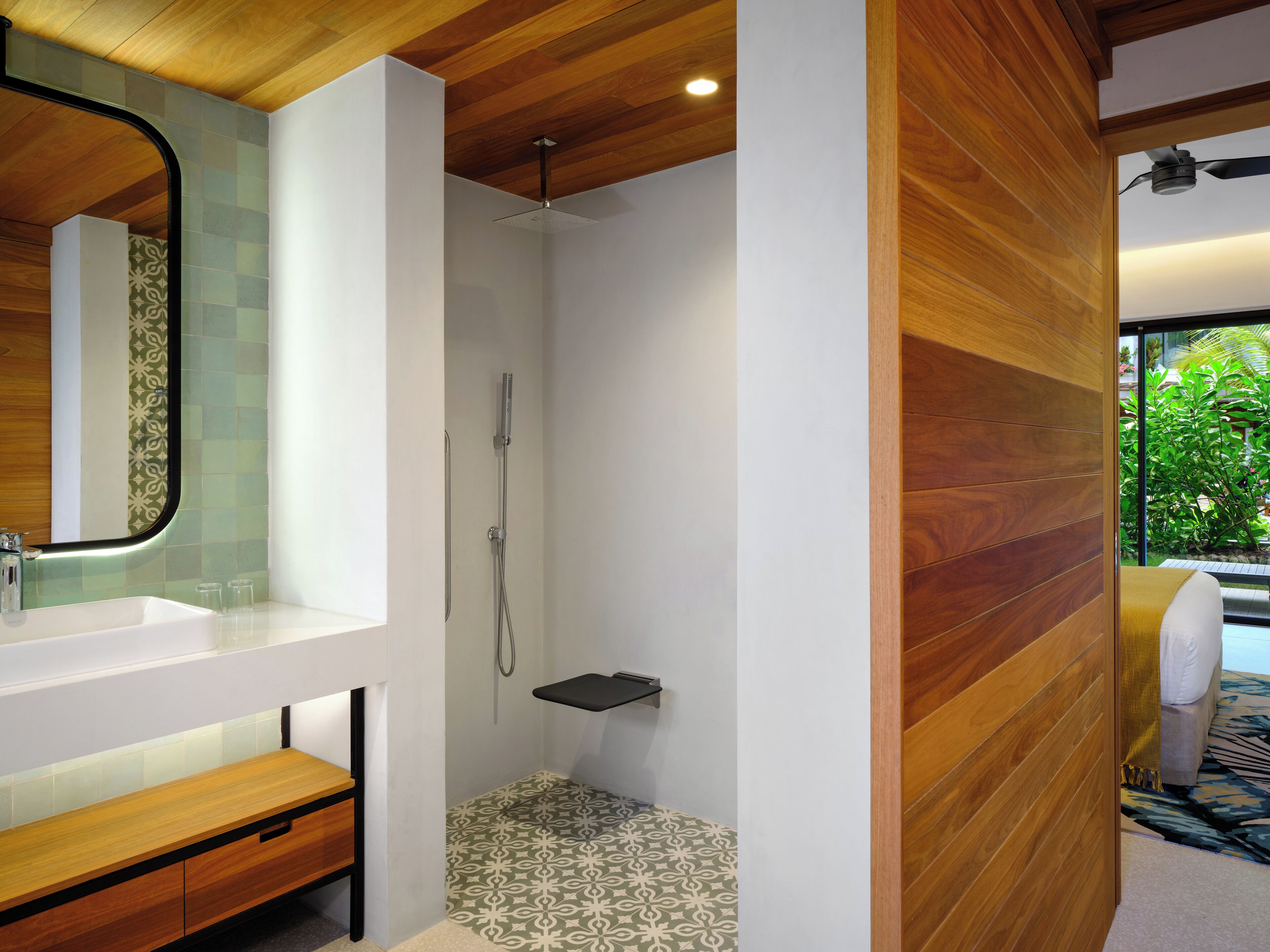 A modern bathroom with a wooden ceiling, a shower with a patterned floor, and a white sink with a mirror.